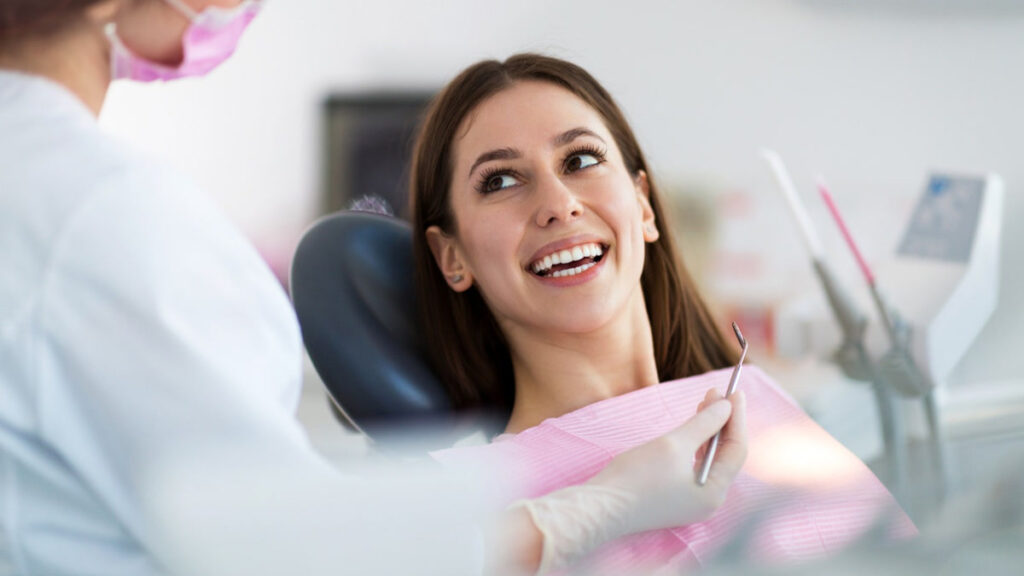 Smiling woman patient with bright healthy smile in a dental chair beside a dentist