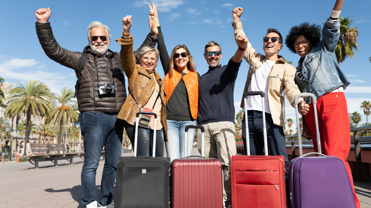 Group of happy travelers with suitcases raising their arms in celebration