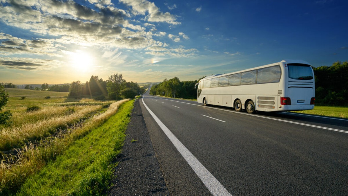 White coach bus driving on a rural highway at sunset