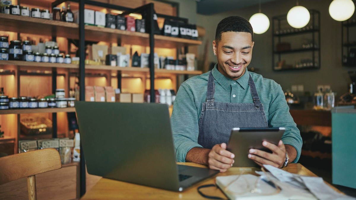 Small business owner working on a laptop and tablet in his shop